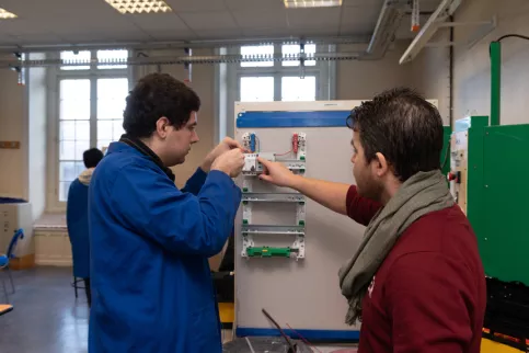 Un jeune et son formateur en électricité travaillent sur un plateau technique