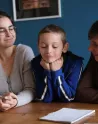 Deux adultes entourent un jeune face à un cahier
